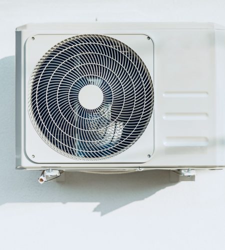 New outside air conditioner unit hanging on white wall, front view