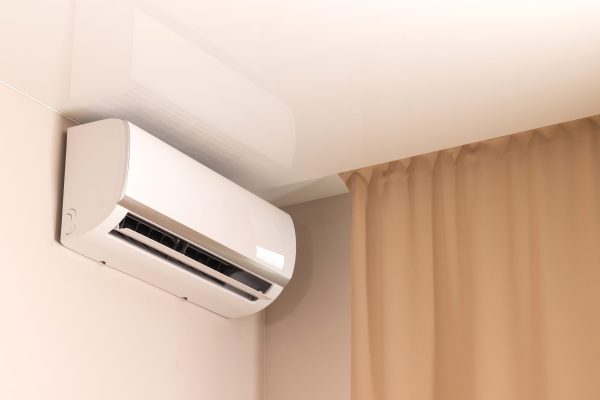 White air conditioner under stretch ceiling in modern room with beige curtains